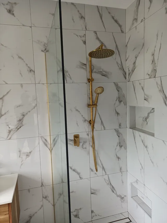 Marble-look tiled shower with brushed brass rain shower head and hand shower