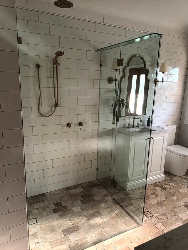 Walk-in glass shower with brass rain head, white subway tiles and terracotta floor tiles