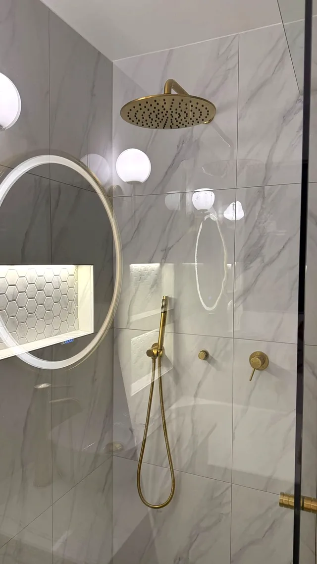 Brushed brass rain shower head, hand shower and mixers against marble-look tiles