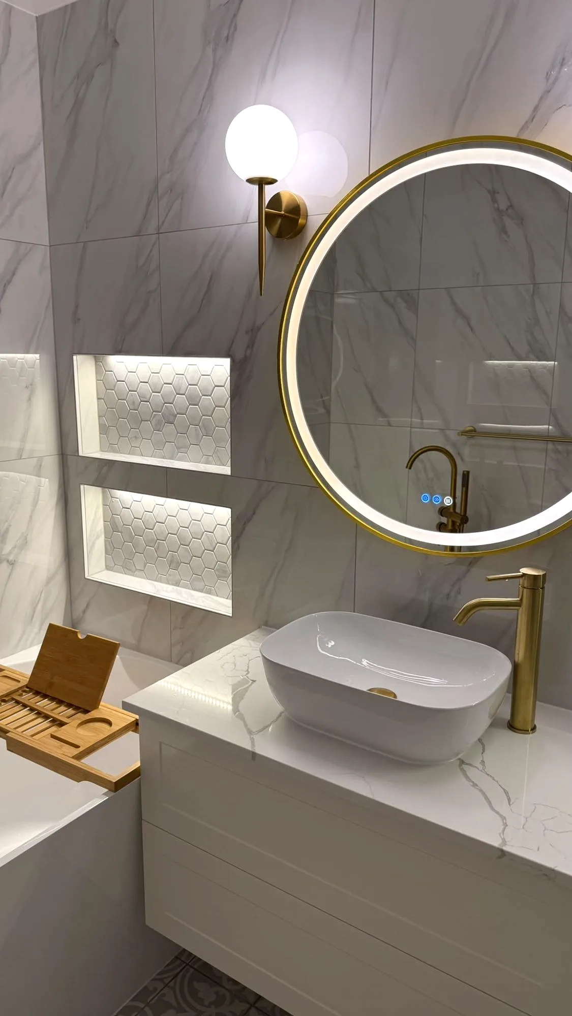 Floating vanity, gold LED mirror and hexagon-mosaic niches on marble-look walls