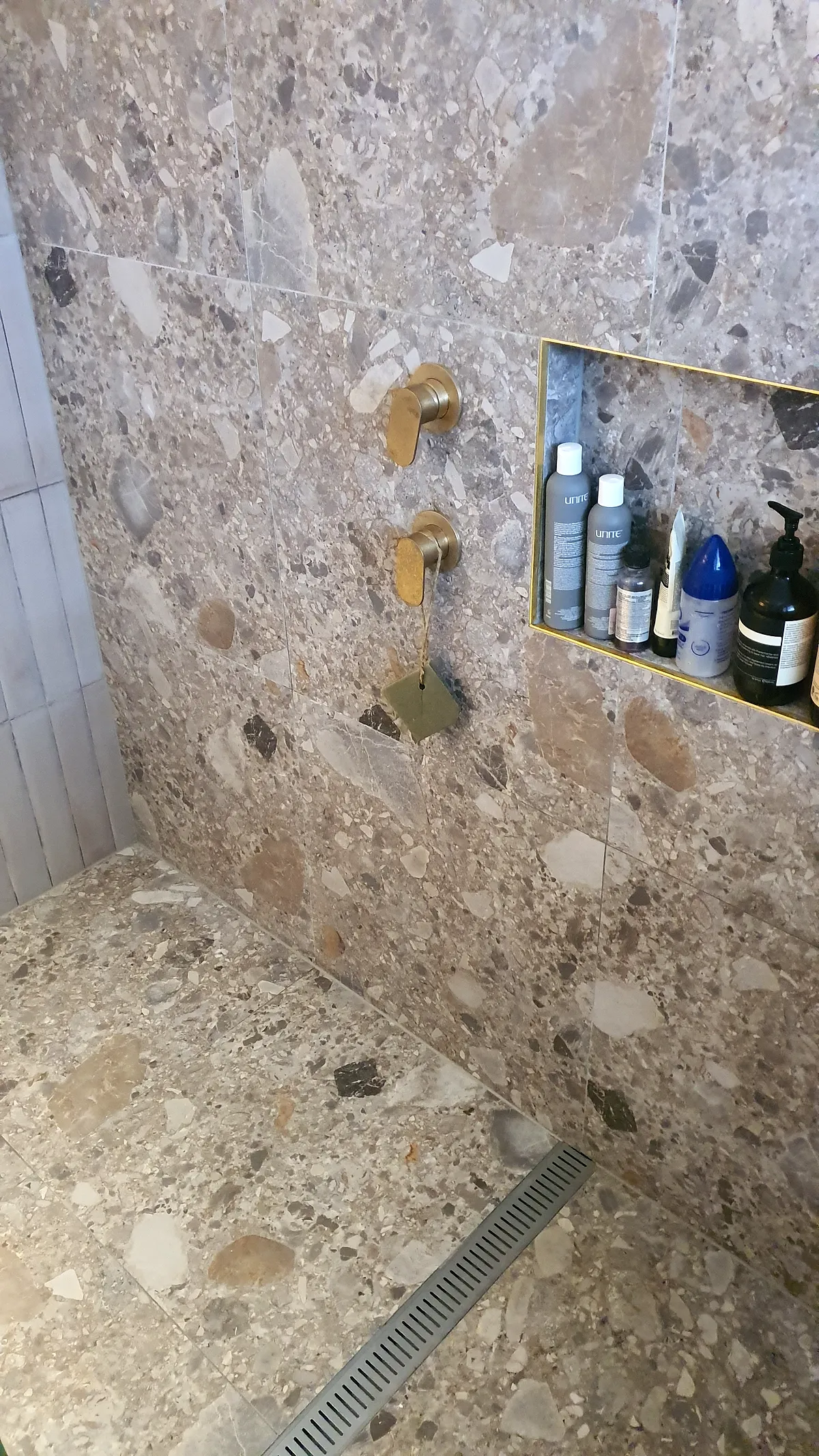 Terrazzo-look shower with brass tapware and a feature niche
